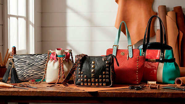 Cinco carteras y bolsos de cuero hechos a mano sobre una mesa de taller